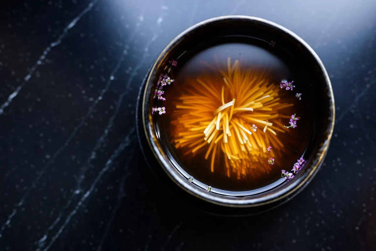 A clear broth in a black bowl with flowers.