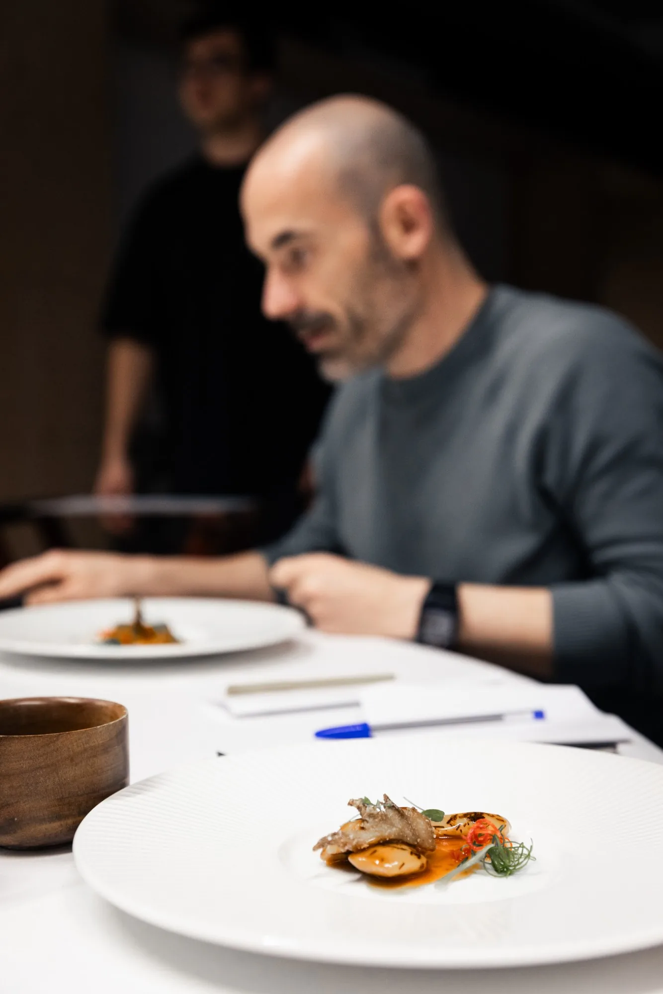 A guest tasting a dish at a tasting session, notebook beside the plate.